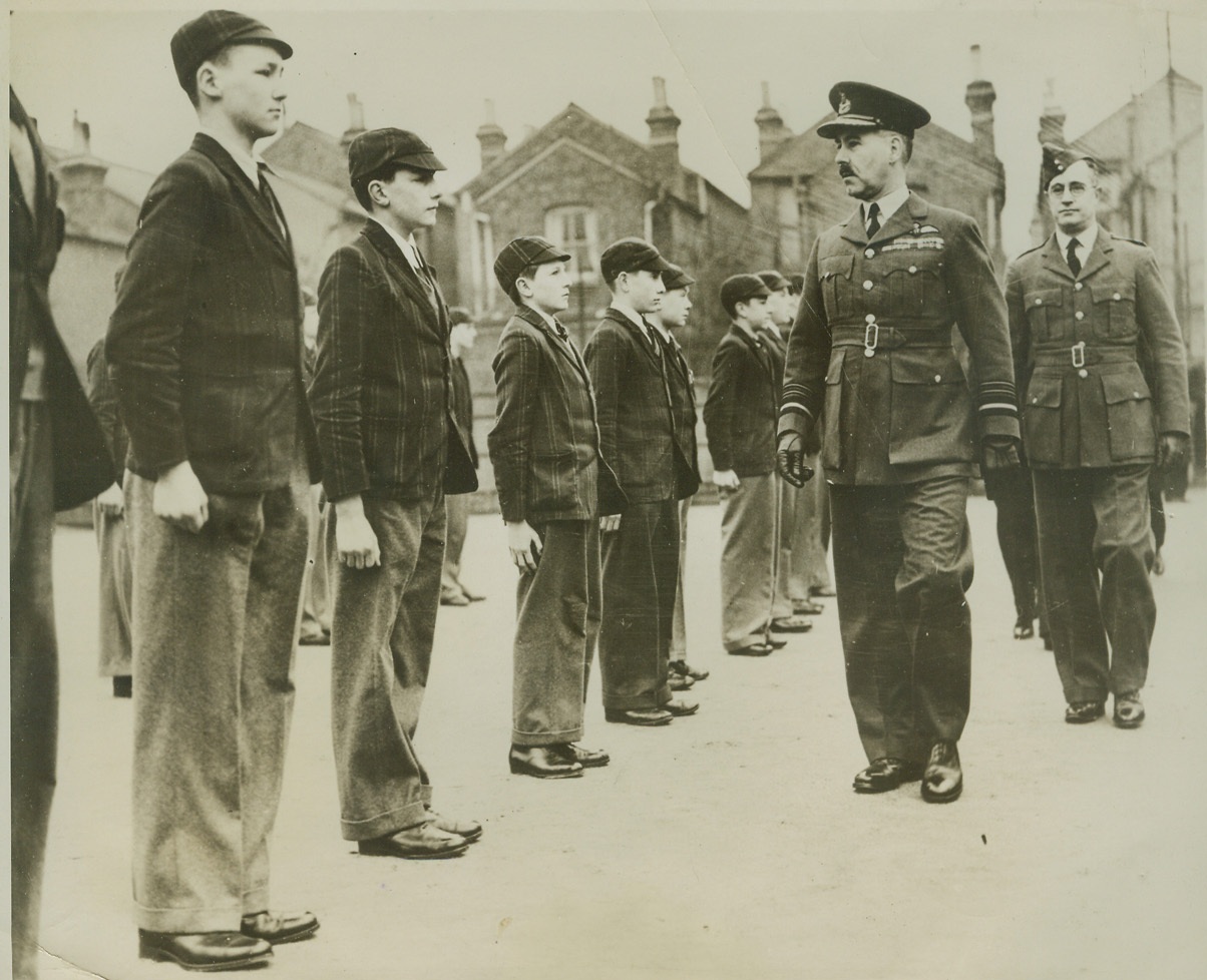 AIR MARSHAL INSPECTS FLIERS OF THE FUTURE, 3/18/41  ENGLAND – Air Marshal A. G. R. Garrod, Air Member for Training, inspects the Tiffin Boys’ School Unit of the Air Training Corps during a recent tour of inspection. The boys, still in their school clothes, stand stiffly at attention. These youngsters are learning the rudiments of flying and may some day, should the war last long enough, take their places in the first line of Britain’s aerial defense. (Passed by British censor). Credit: ACME;