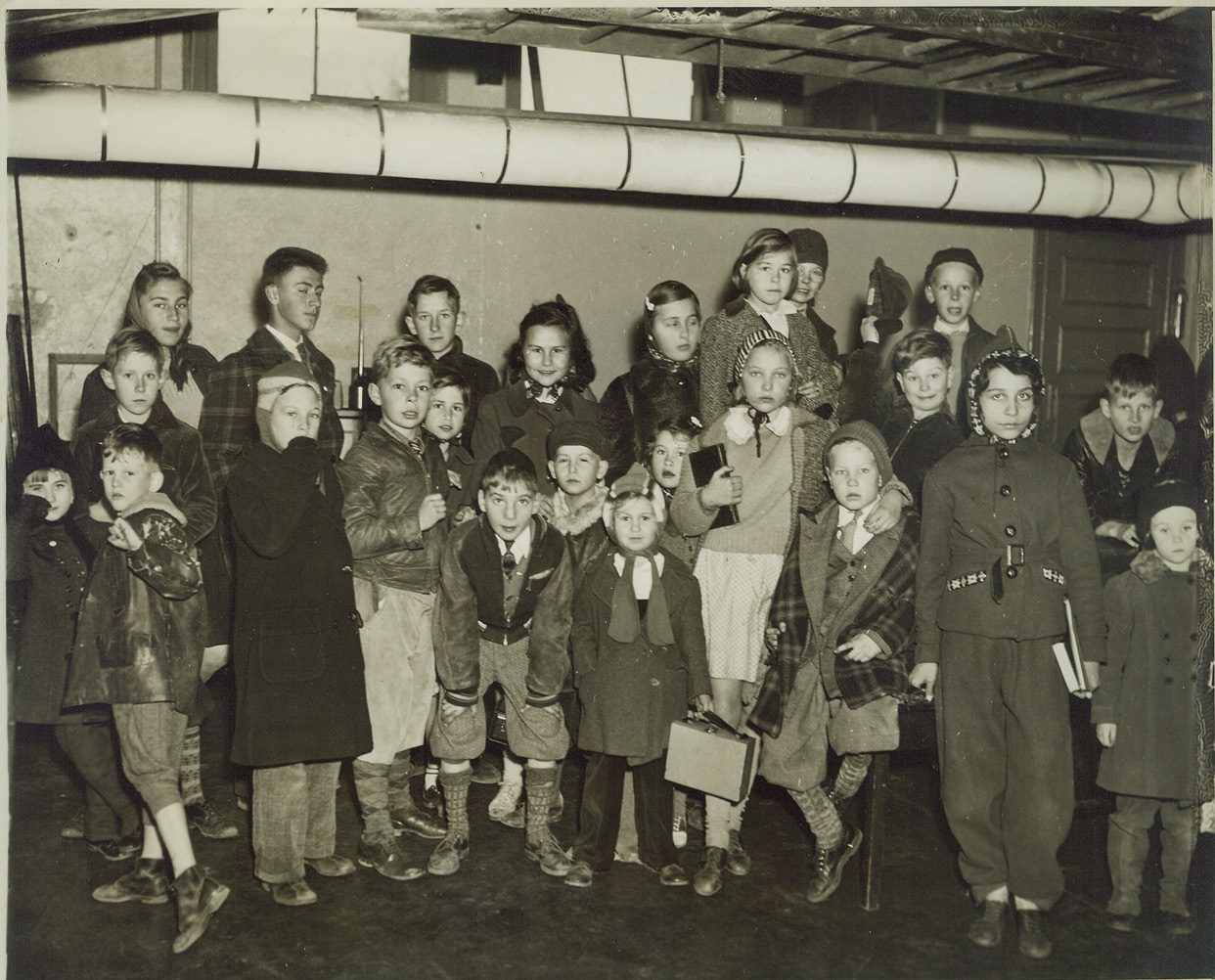 SCHOOL BASEMENT “SHELTER” FOR CHILDREN, 12/9/41  HEMPSTEAD, N.Y.: These youngsters, principally children of non-commissioned officers at Mitchell Field, were herded into the basement of the Washington School, Washington Street and Van Cott Avenue, when an air raid alarm was sounded, December 9. Women and children have been evacuated from Mitchell Field, which made it necessary to keep these youngsters in school while others were sent home in orderly manner. War Department officials later said the alarm resulted from a “phony” tip. Credit: OWI Radiophoto from ACME;