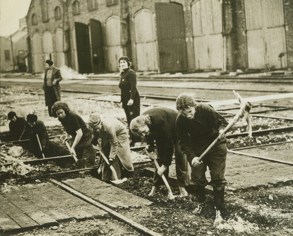 Women’s Pick and Shovel Gang Lays Power Cable, 12/9/41  Southern England – Women swing picks and heft shovels, digging trenches and laying a power cable at a Southern Railway Depot in England. England’s acute shortage of manpower has caused officials to ask women to volunteer for this work. The English censor’s caption on the photo remarks, “The work is said to be as good and to be proceeding even quicker than under normal conditions with men worker.” Credit: ACME;