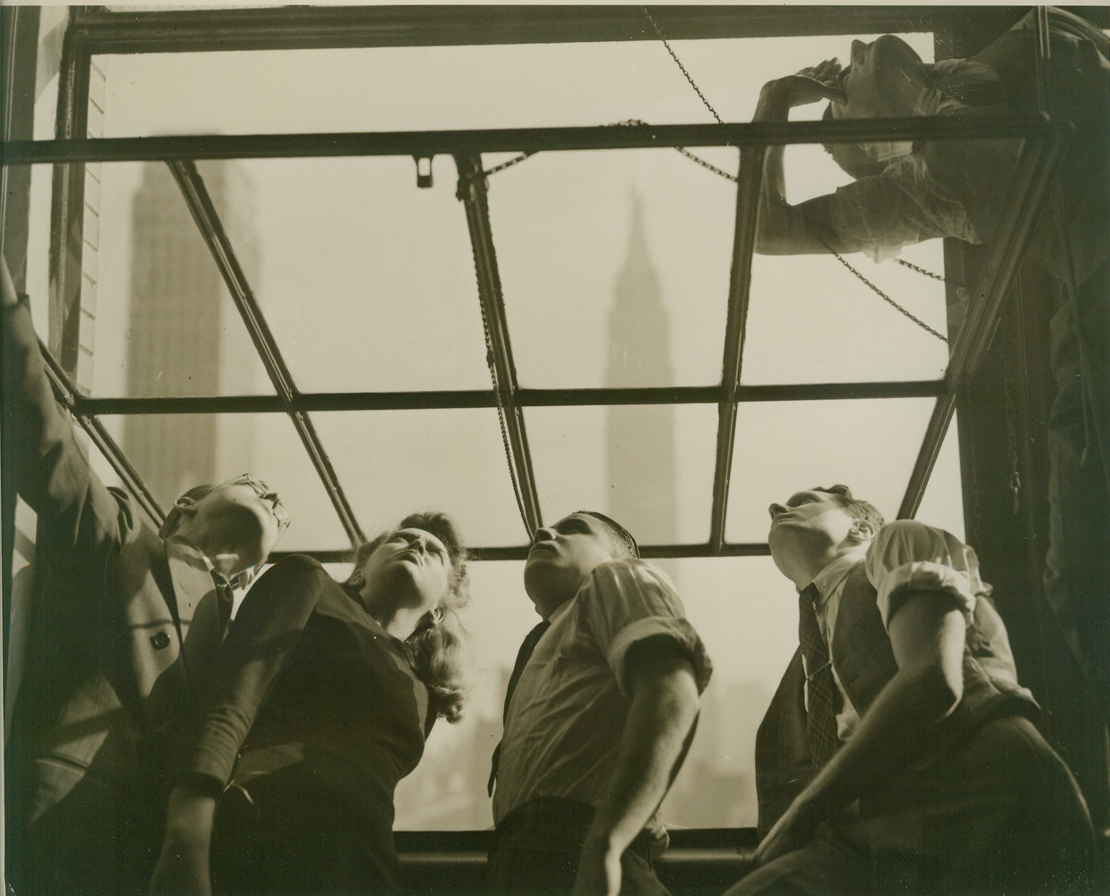 LOOKING FOR INVADERS, 12/10/41  NEW YORK – This morning (Dec. 10) air raid sirens started blowing in this city. Office workers, having just arrived at their place of employment in midtown, scampered to the window and peered skyward, looking for enemy planes. The alarm was shortlived, however, the all clear being announced within a few moments. Directly in the background can be seen the World’s Tallest Building – The Empire State Bldg. Credit: OWI Radiophoto from ACME;